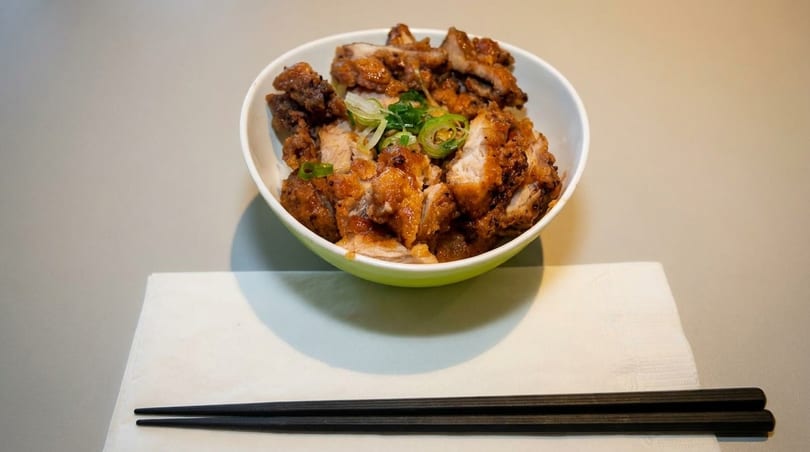 Bowl of crispy fried chicken pieces topped with green onions, served with black chopsticks.
