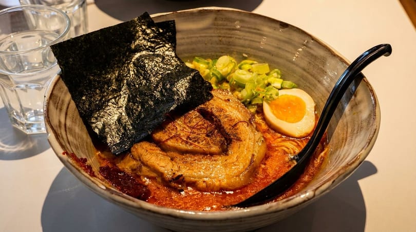 Spicy ramen bowl with pork belly, soft-boiled egg, scallions, and nori seaweed.
