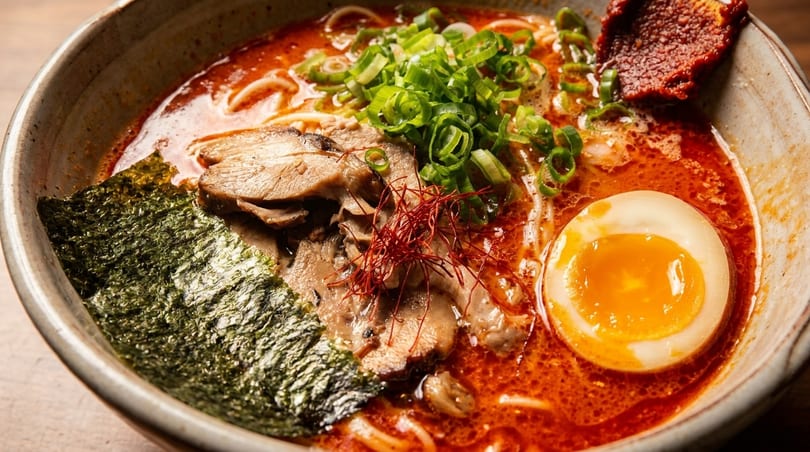 Spicy ramen bowl with rich red broth, pork, soft-boiled egg, green onions, and nori.